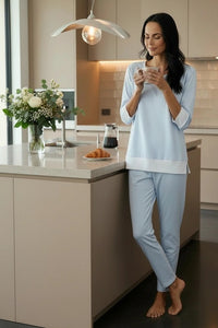 Woman in pajamas standing in a modern kitchen holding a cup.